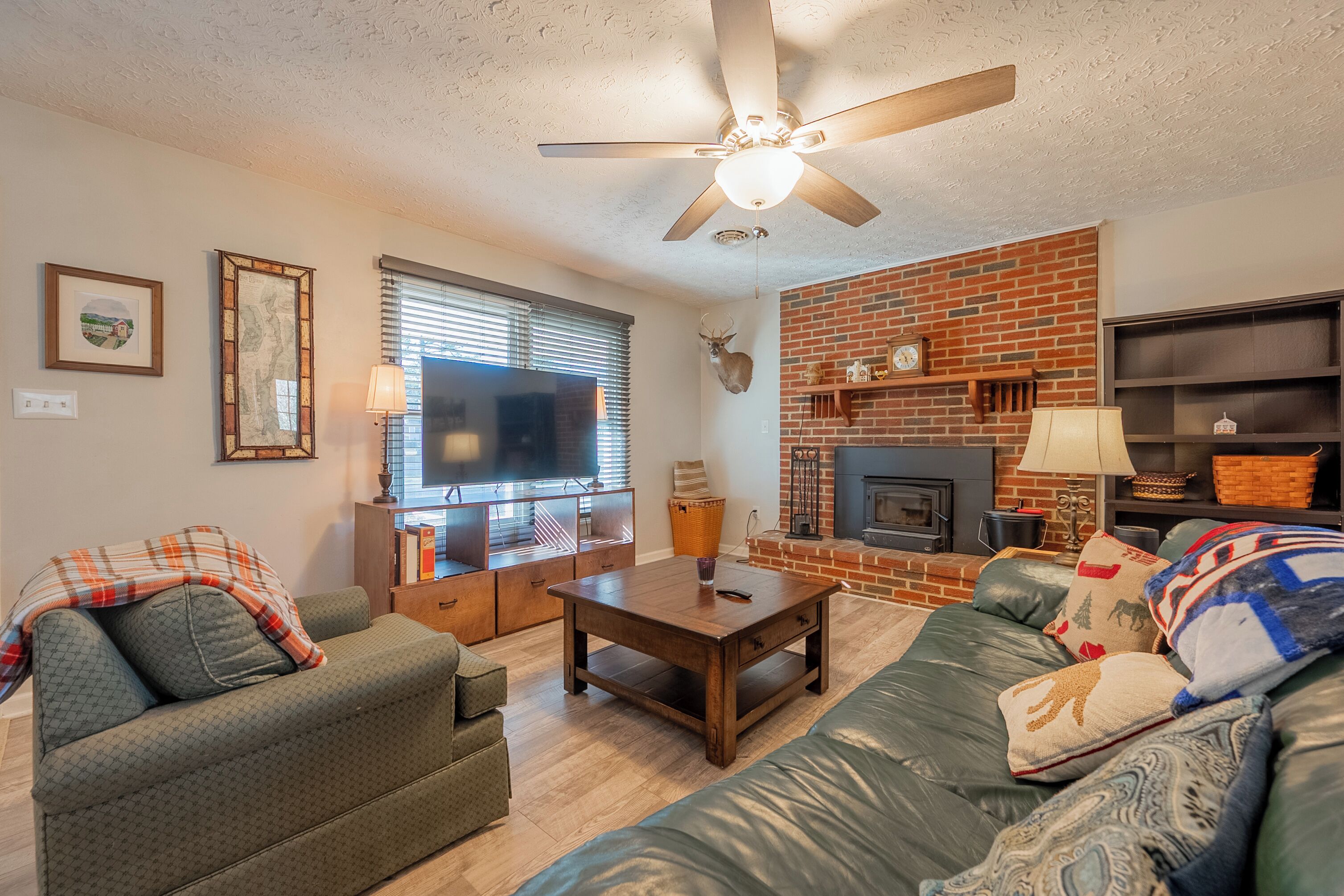 A living room with a brick fireplace, a ceiling fan, and a television.