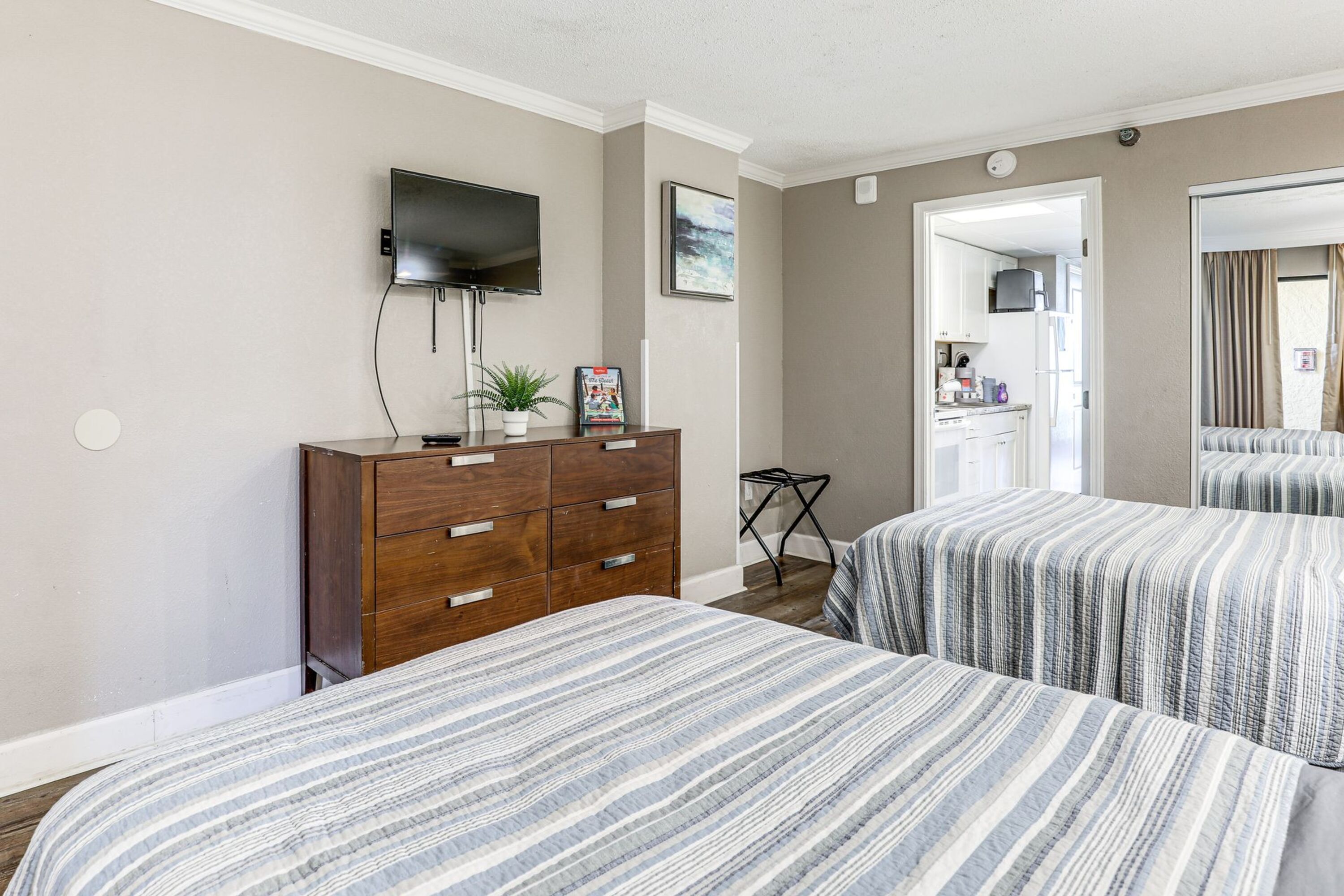 A hotel room with two beds, a wooden dresser, a flat-screen TV, and a door leading to a bathroom.
