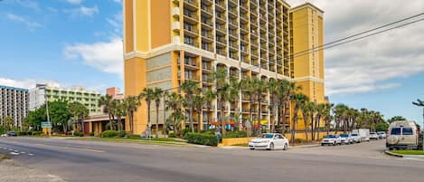 A multi-story hotel with a yellow facade, balconies, and palm trees in front.
