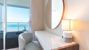 A modern hotel room with a large window offering a view of the sea, a round mirror, a bedside table with a lamp, and a comfortable chair. - Pearl View by Atlantic Holiday (Funchal)