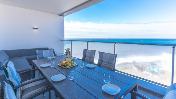 A balcony with a wooden table set for dining, overlooking a clear blue sea. - Pearl View by Atlantic Holiday (Funchal)
