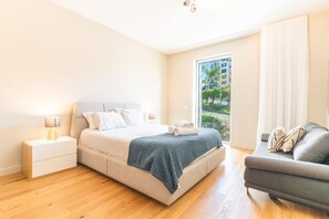 Ein modernes Schlafzimmer mit Bett, Nachttischen, einer Couch und Blick ins Freie.
