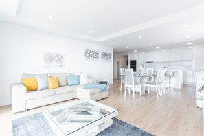 Una sala de estar moderna con un sofá blanco, una mesa de centro de vidrio y un comedor con sillas blancas y una mesa de vidrio.