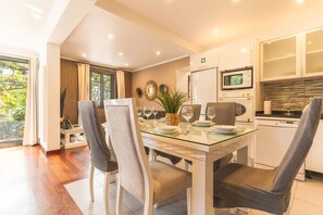 A modern kitchen with a dining area, featuring a glass table, chairs, and a view of the outdoors. - Villa Paixão by Atlantic Holiday (Machico)