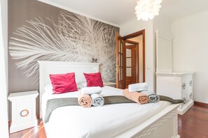 A neatly made bed with red and white pillows, a large decorative wall piece, and a wooden door. - Villa Paixão by Atlantic Holiday (Machico)