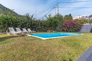 Ein Schwimmbecken mit einer Rasenfläche, weißen Liegestühlen und einem Rettungsring.