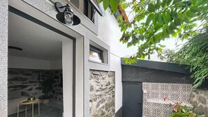 Il s’agit d’un bâtiment moderne avec une façade en pierre, une petite fenêtre et une porte. On peut voir un pot de fleurs et une chaise en métal à l’extérieur.