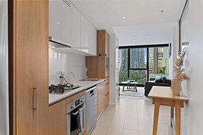 A modern kitchen with wooden cabinets, a gas stove, and a dining area with a table and chairs. - ST Apartments by Arvia Living (Brisbane City)