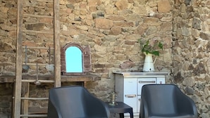 Un mur de pierre avec une échelle en bois, une petite table avec un vase et deux chaises.