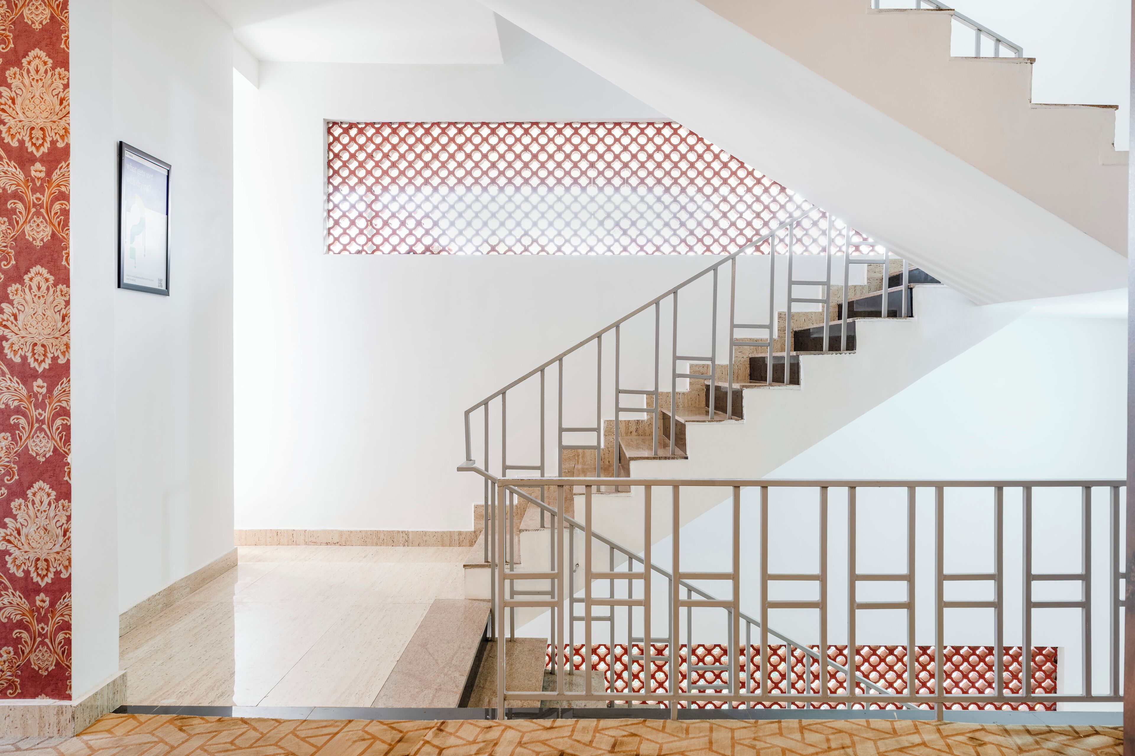 Una escalera con barandilla metálica, pared con diseño y suelo de baldosas.