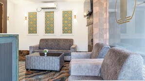 Una hall con pavimento in marmo, divani rivestiti in grigio, un tavolino da caffè e pannelli decorativi alle pareti.