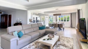 A spacious living area with a large beige sectional sofa, a coffee table, and a dining area with a table and chairs. - Villa Baradaye by Atlantic Holiday (Calheta)
