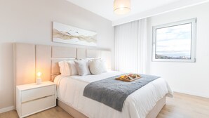 Egy modern hálószoba, melyben egy nagy ágy, egy éjjeliszemélyzet lámpával, egy ablakon át nyíló kilátás a városra, és egy absztrakt műalkotás díszíti a falat.