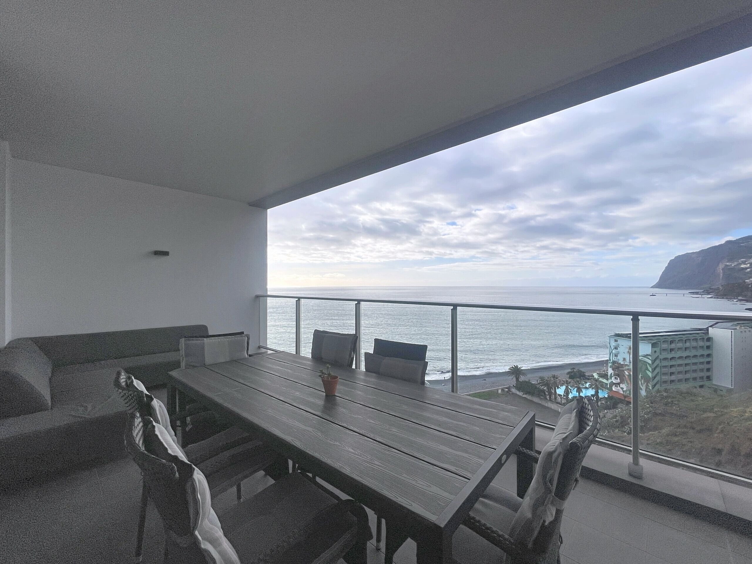 Un balcon avec une table et des chaises en bois, offrant une vue sur la côte, avec des bâtiments et des falaises.