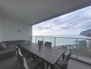 A balcony with a wooden table and chairs, overlooking a coastal view with buildings and cliffs. - Pearl View by Atlantic Holiday (Funchal)