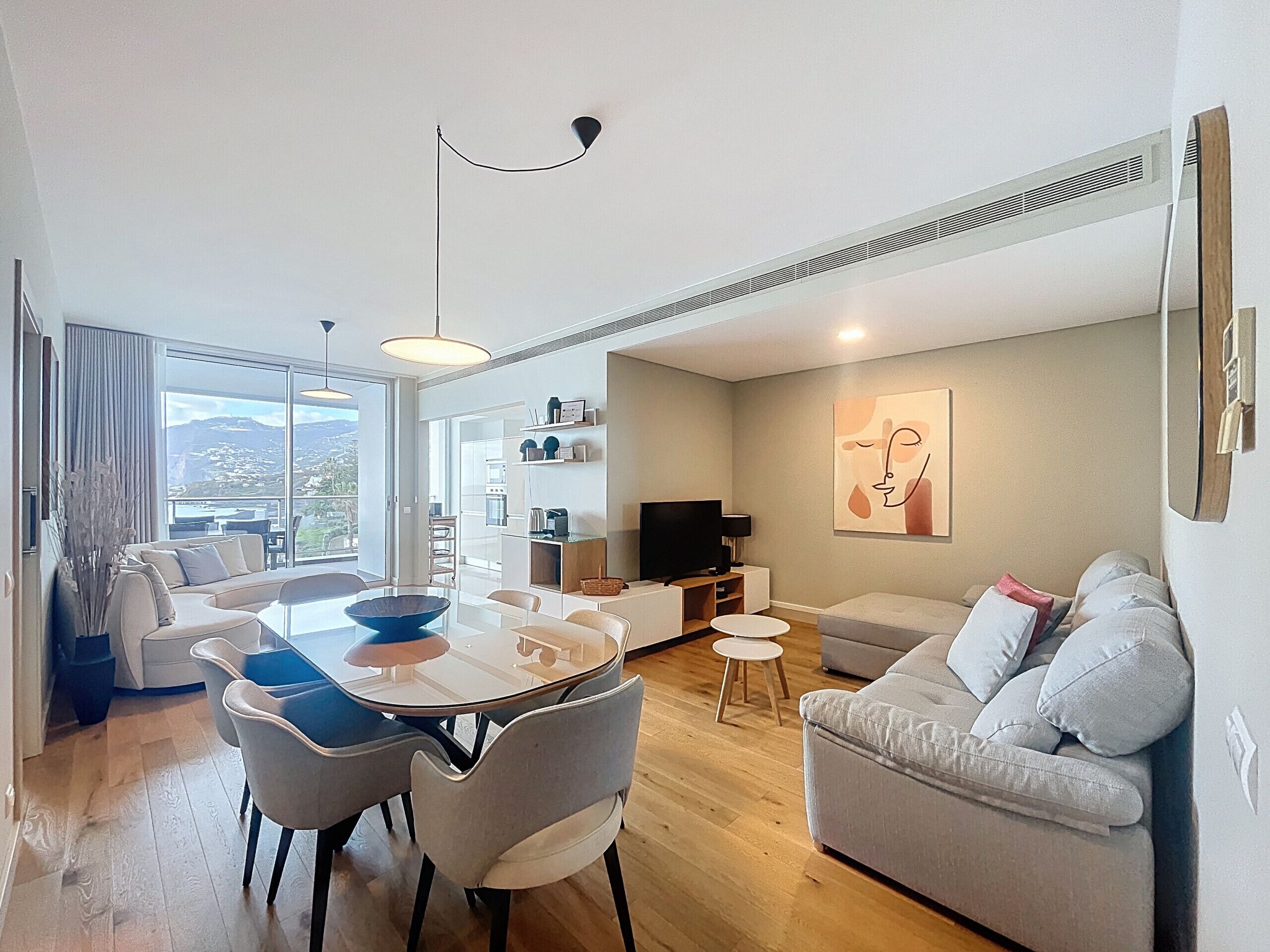 A modern living room with a dining area, a sofa, a TV, and artwork on the wall.