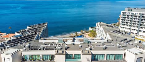 A modern building with a rooftop terrace, a pool, and a view of the ocean.