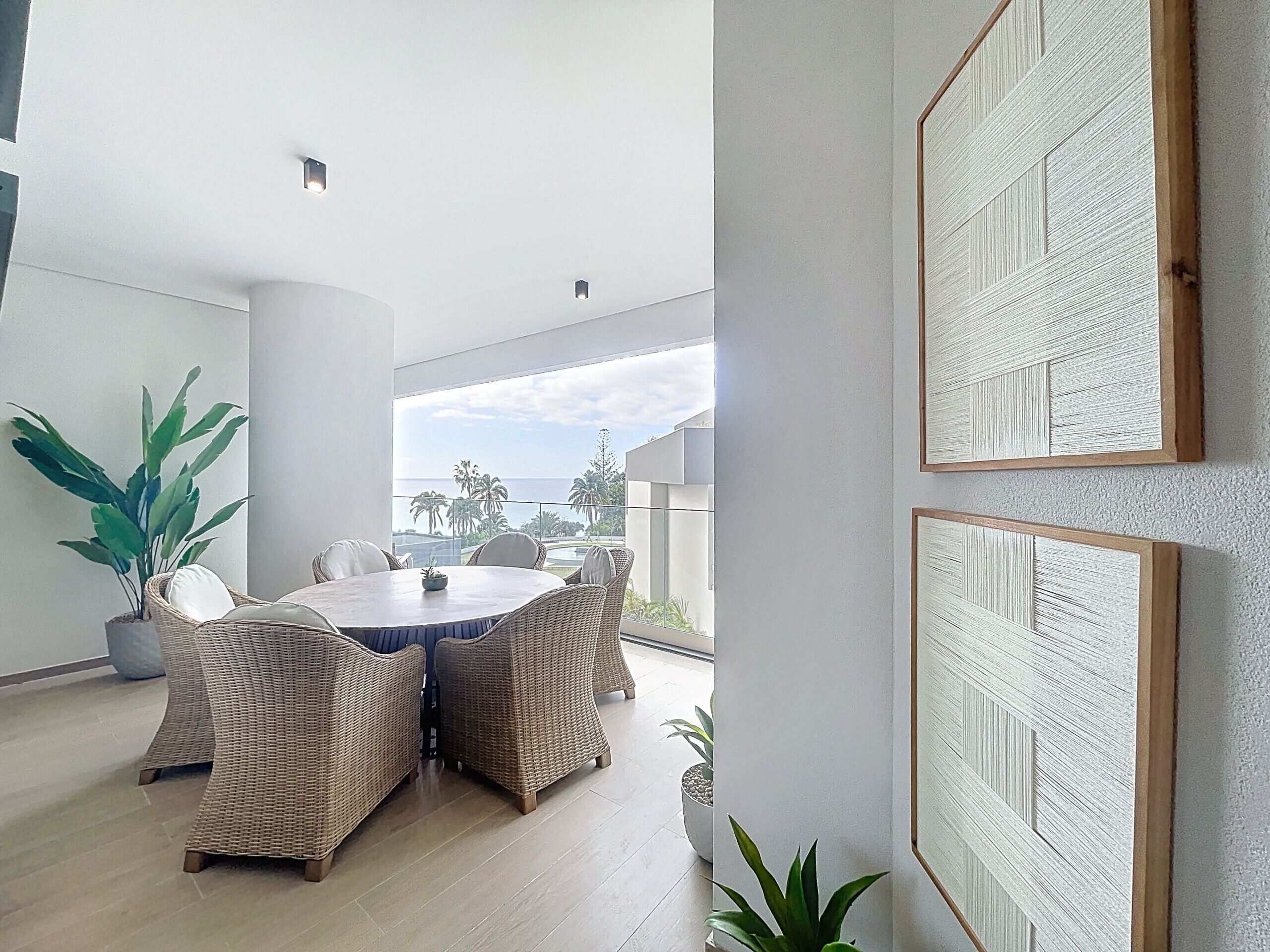 A modern dining area with wicker furniture, a round table, and a view of the ocean.