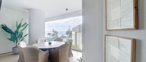 A modern dining area with wicker furniture, a round table, and a view of the ocean.