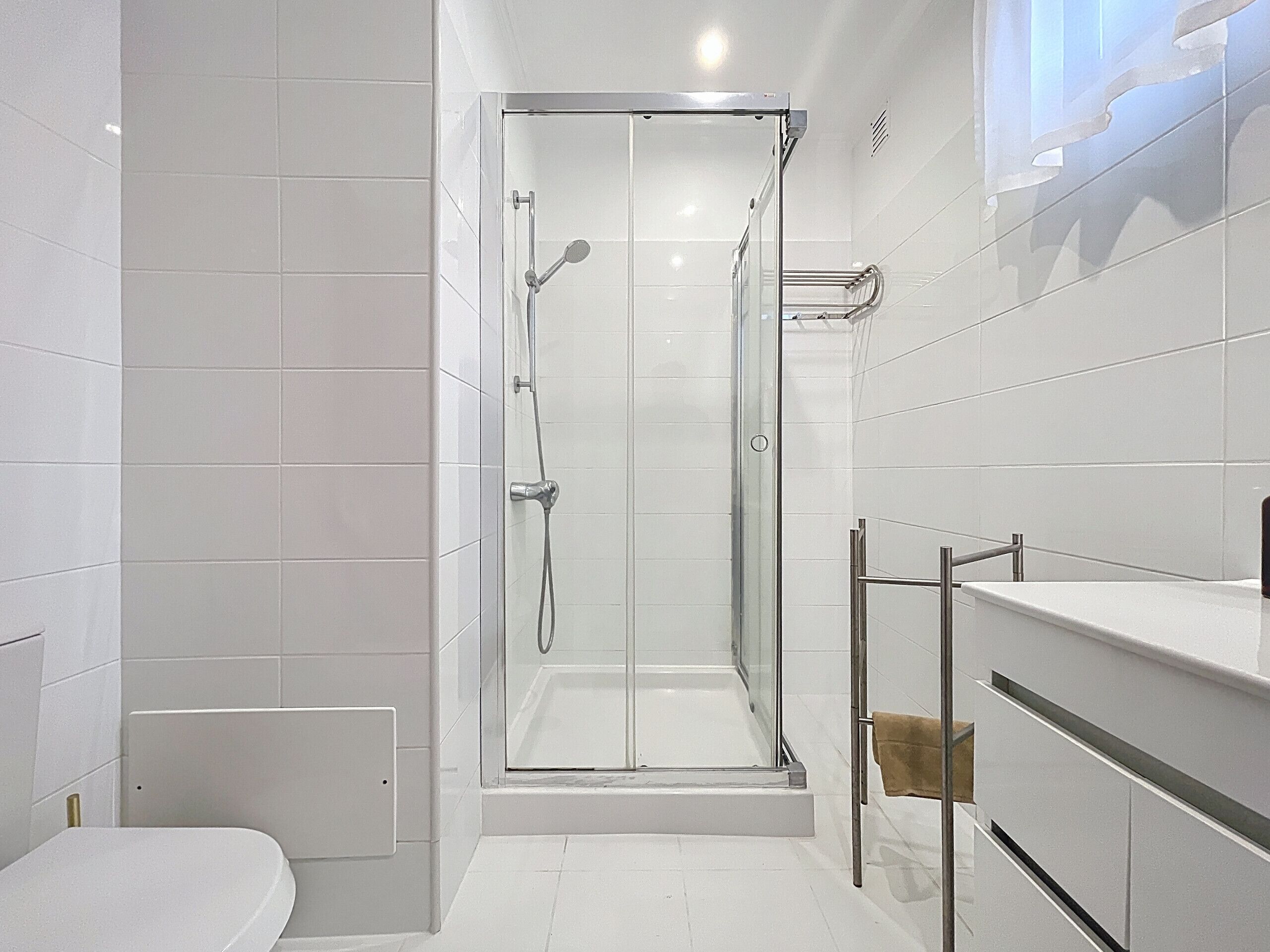 A modern bathroom with a glass-enclosed shower, white tiled walls, and a white toilet.