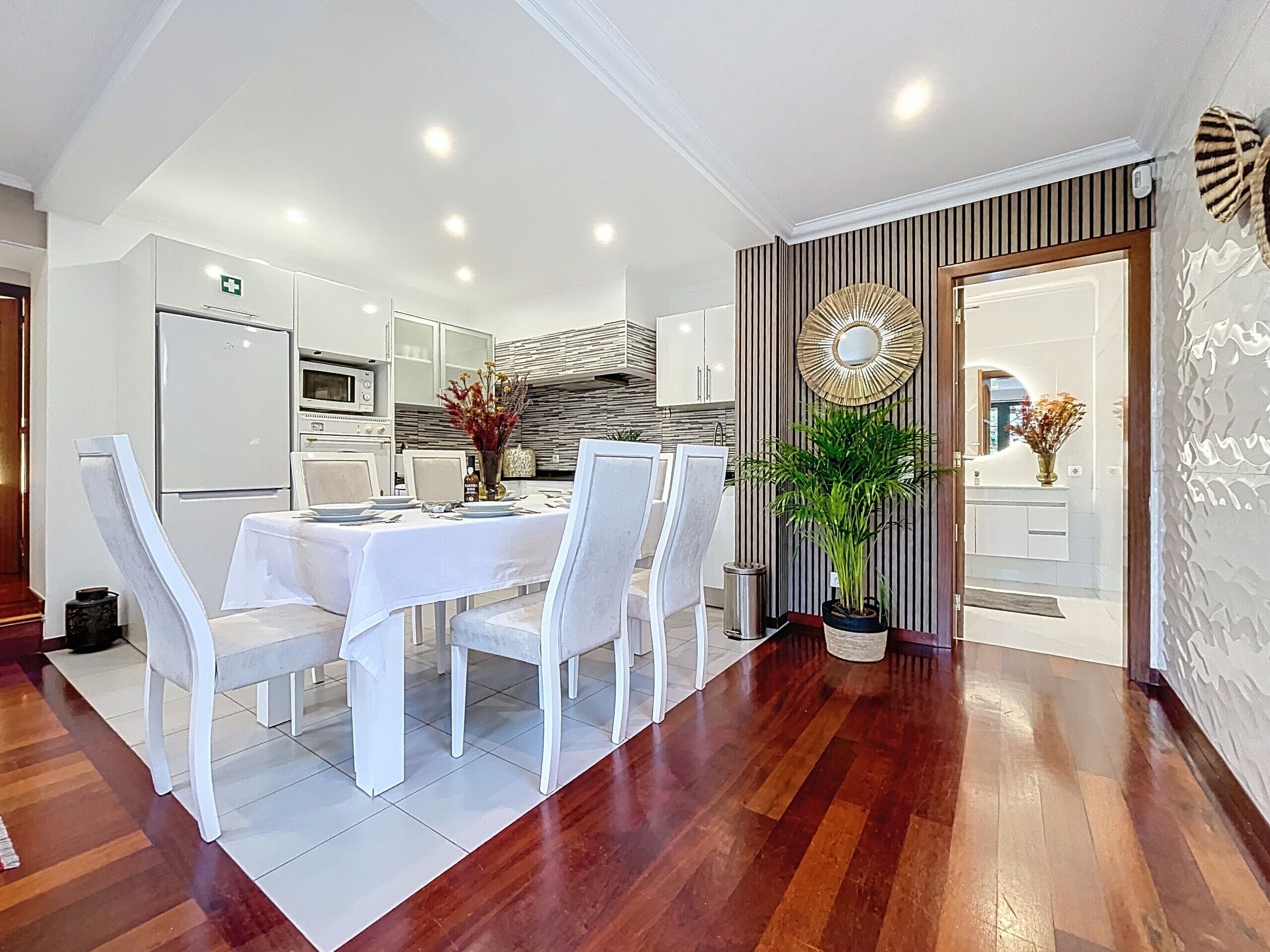 A modern kitchen with white cabinetry, a dining area with a white table and chairs, and a potted plant.