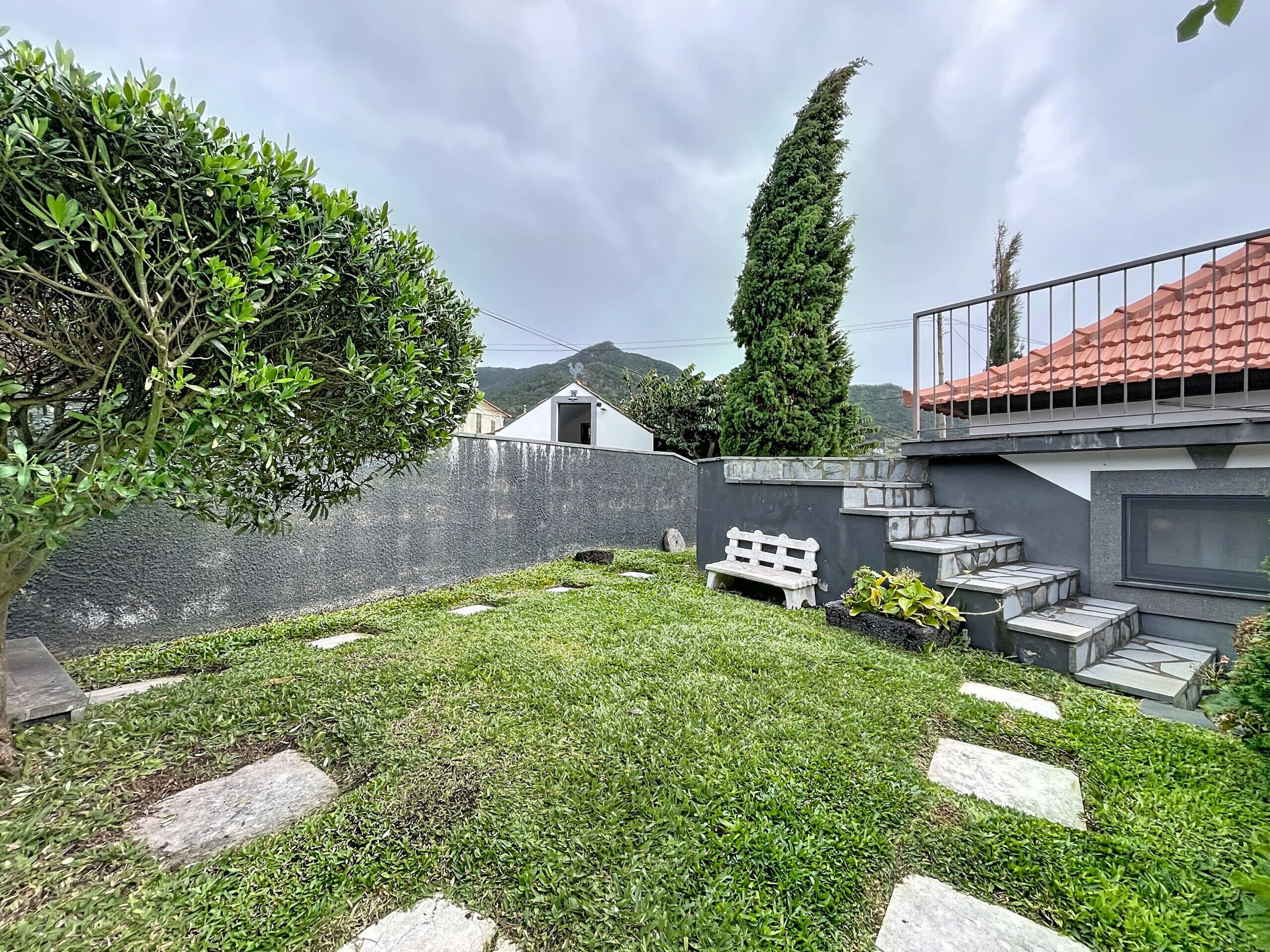 A modern house with a well-maintained lawn, a white bench, and a tall tree.