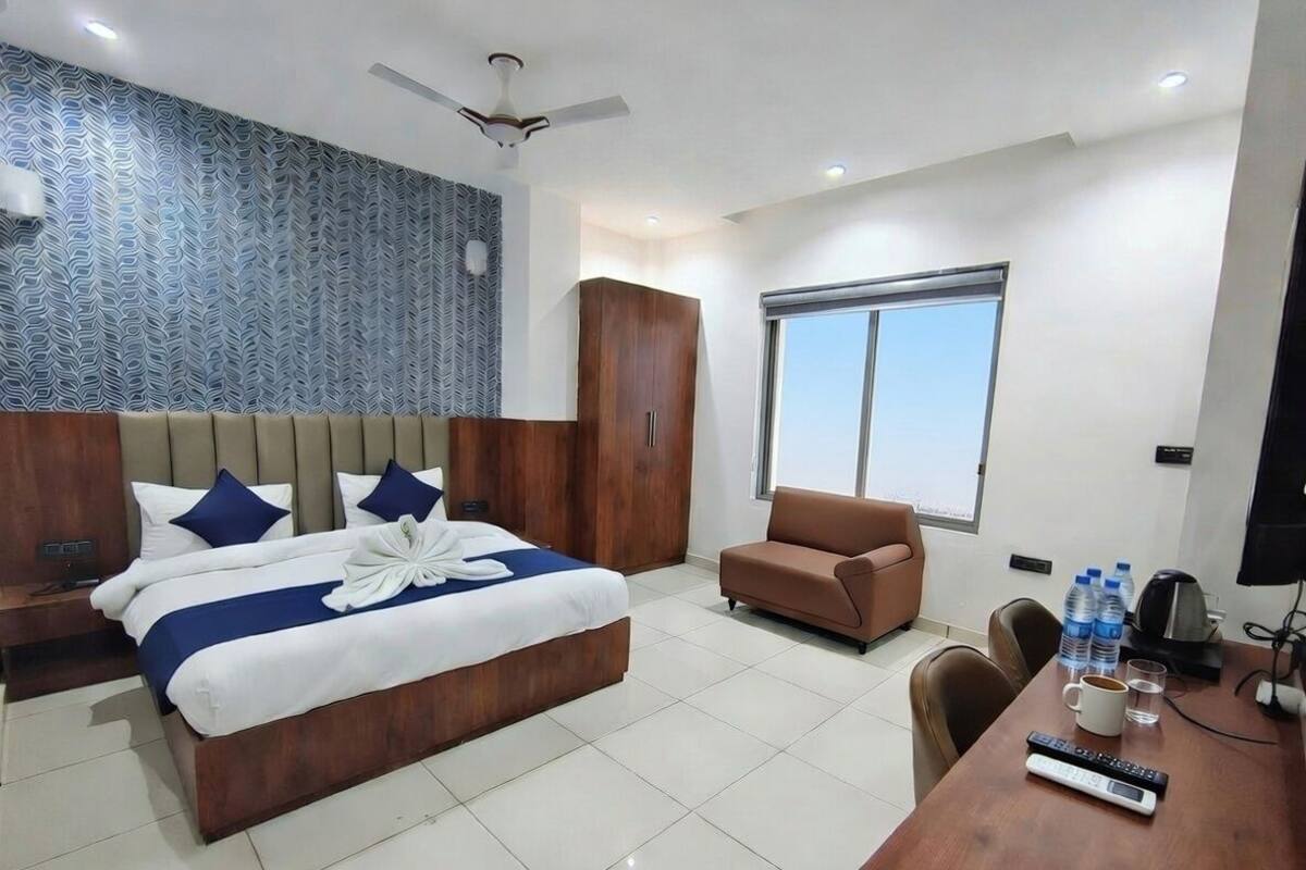 Une chambre d’hôtel avec un grand lit, un canapé, un bureau avec un ordinateur et une fenêtre.