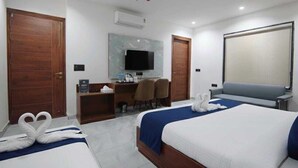 A hotel room with two beds, a desk with a chair, a television, and a ceiling fan. - Belle Tree Hotel (Greater Noida)