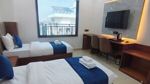 A hotel room with two beds, a desk, a TV, and a balcony with solar panels. - Belle Tree Hotel (Greater Noida)