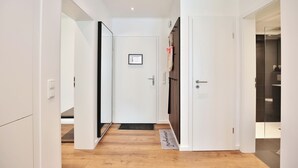 Un pasillo con paredes blancas, piso de madera y una puerta con picaporte negro.