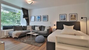Un dormitorio moderno con cama, sofá, una mesa de centro y una ventana con cortinas. Hay cuatro cuadros enmarcados en la pared.