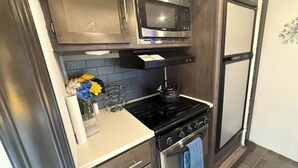 A compact kitchen with a microwave, stove, and oven. There is a vase with flowers on the counter.