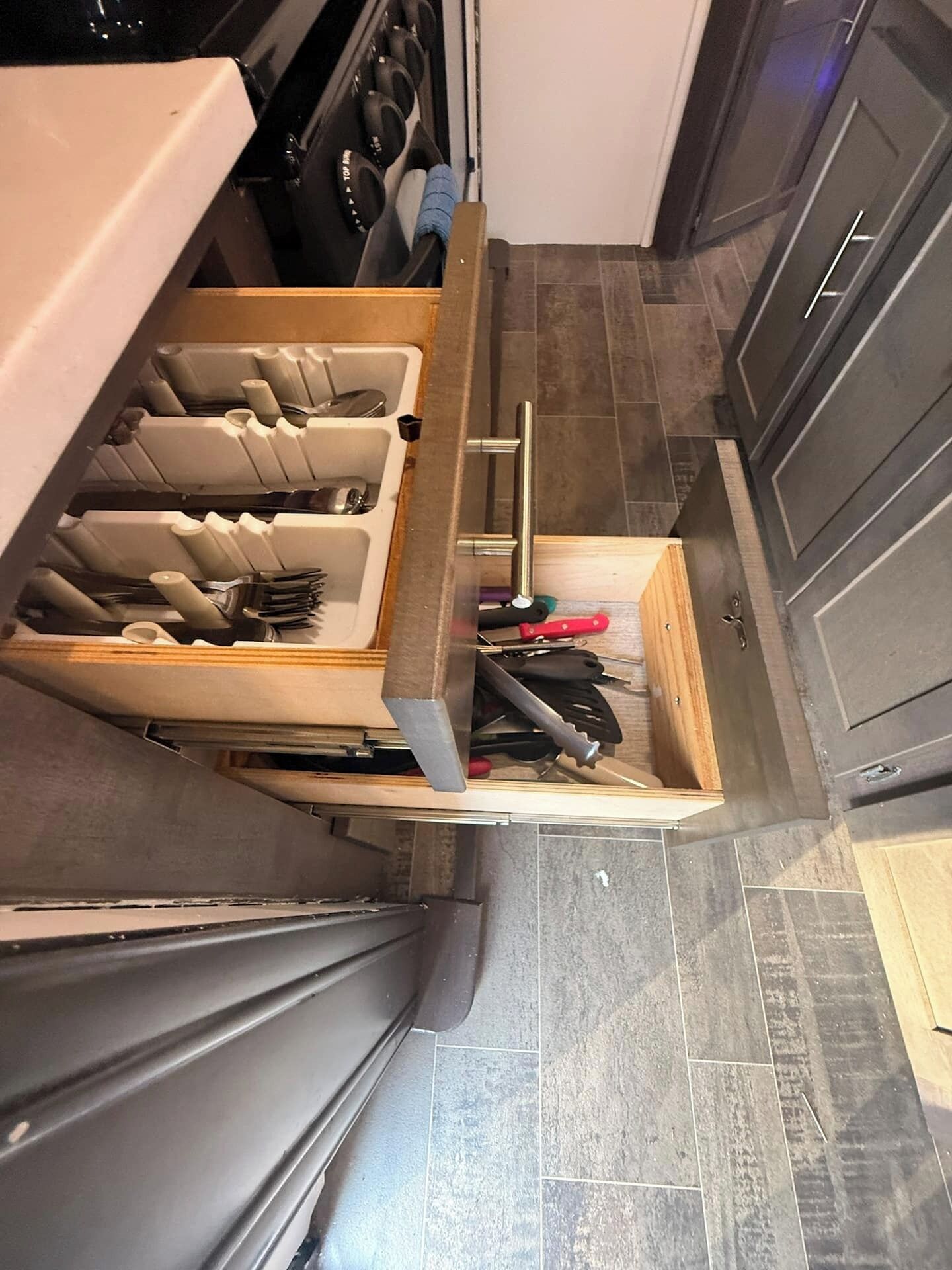 A kitchen with a drawer organizer containing utensils and a cutting board.