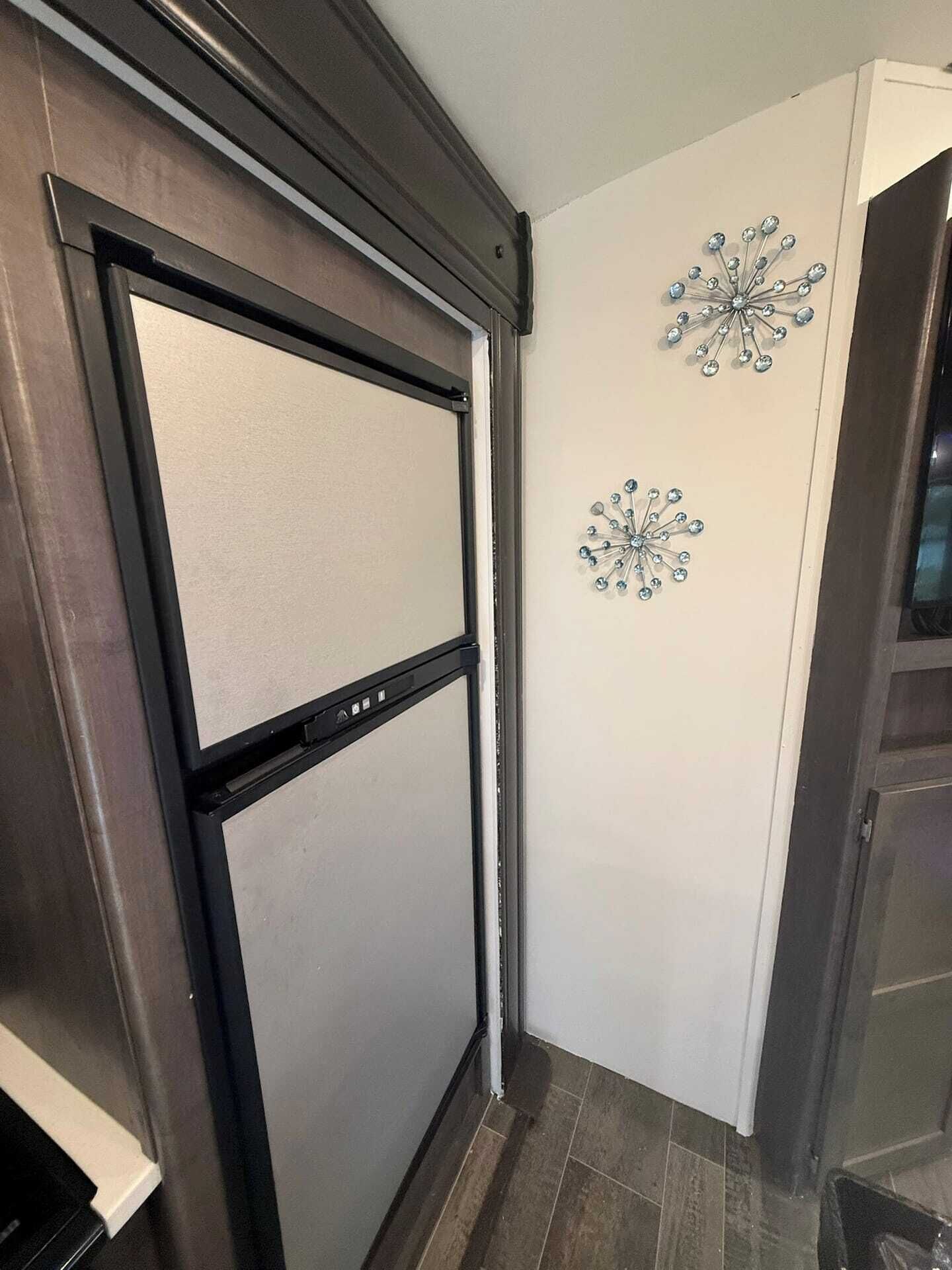 A modern kitchen with a black-framed refrigerator, white walls, and decorative metallic wall art.