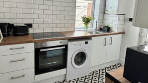 Una cocina moderna con azulejos blancos tipo metro, campana extractora negra, horno empotrado, lavadora y ventana con vistas a edificios.