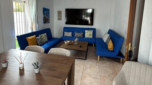 Un soggiorno con un divano blu, un tavolino in legno, una TV a parete e una ventola a soffitto.