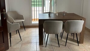 Zona pranzo con tavolo in legno, quattro sedie, una ventola a soffitto e vista esterna tramite una porta vetrata.