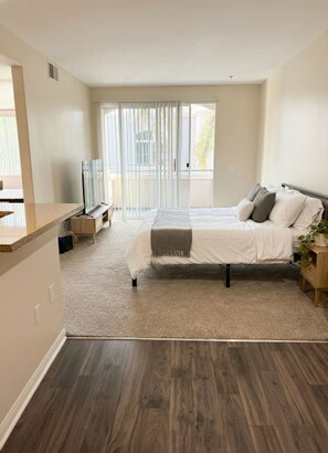 Een moderne slaapkamer met een groot bed, een televisie en een schuifdeur naar een balkon.