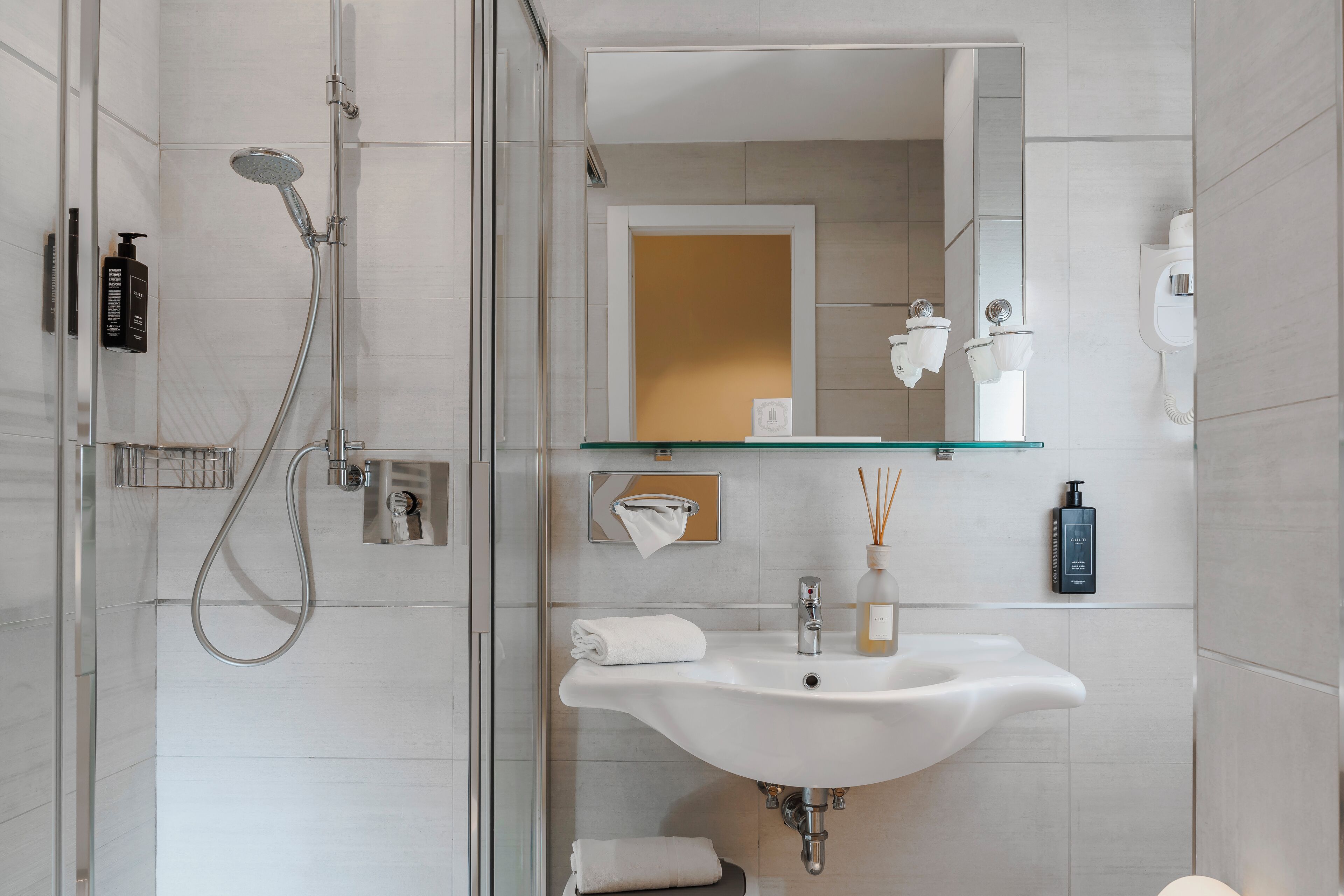 Un baño moderno con cabina de ducha de vidrio, un lavamanos blanco con espejo y artículos de aseo colgados en la pared.