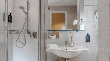 Un baño moderno con cabina de ducha de vidrio, un lavamanos blanco con espejo y artículos de aseo colgados en la pared.