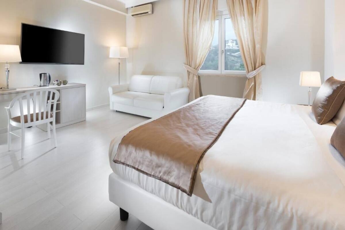 A modern hotel room with a large bed, a desk, a chair, and a TV mounted on the wall.