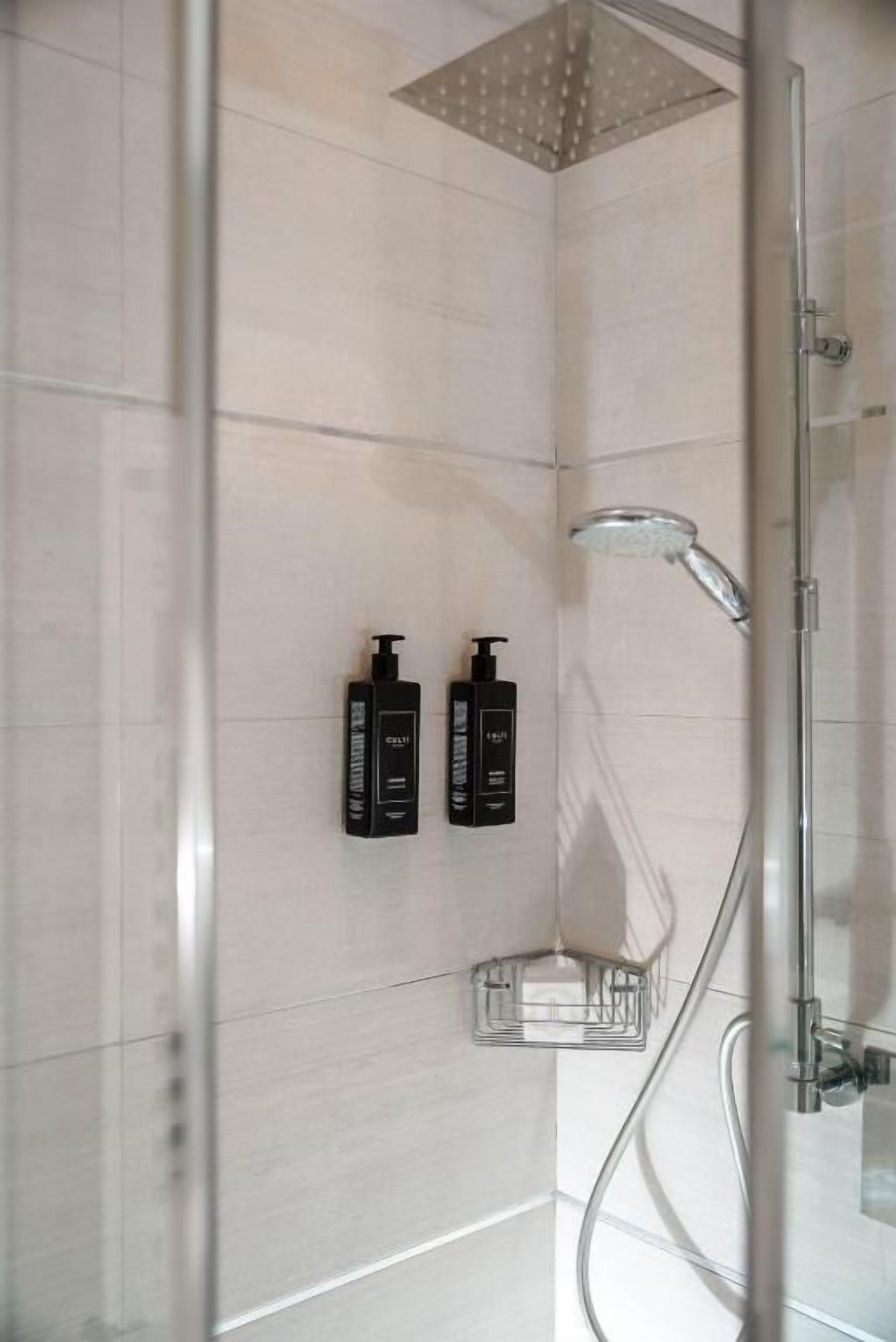 Ducha moderna con cerramiento de vidrio, cabezal de ducha manual y dos botellas de artículos de aseo negro en la pared.