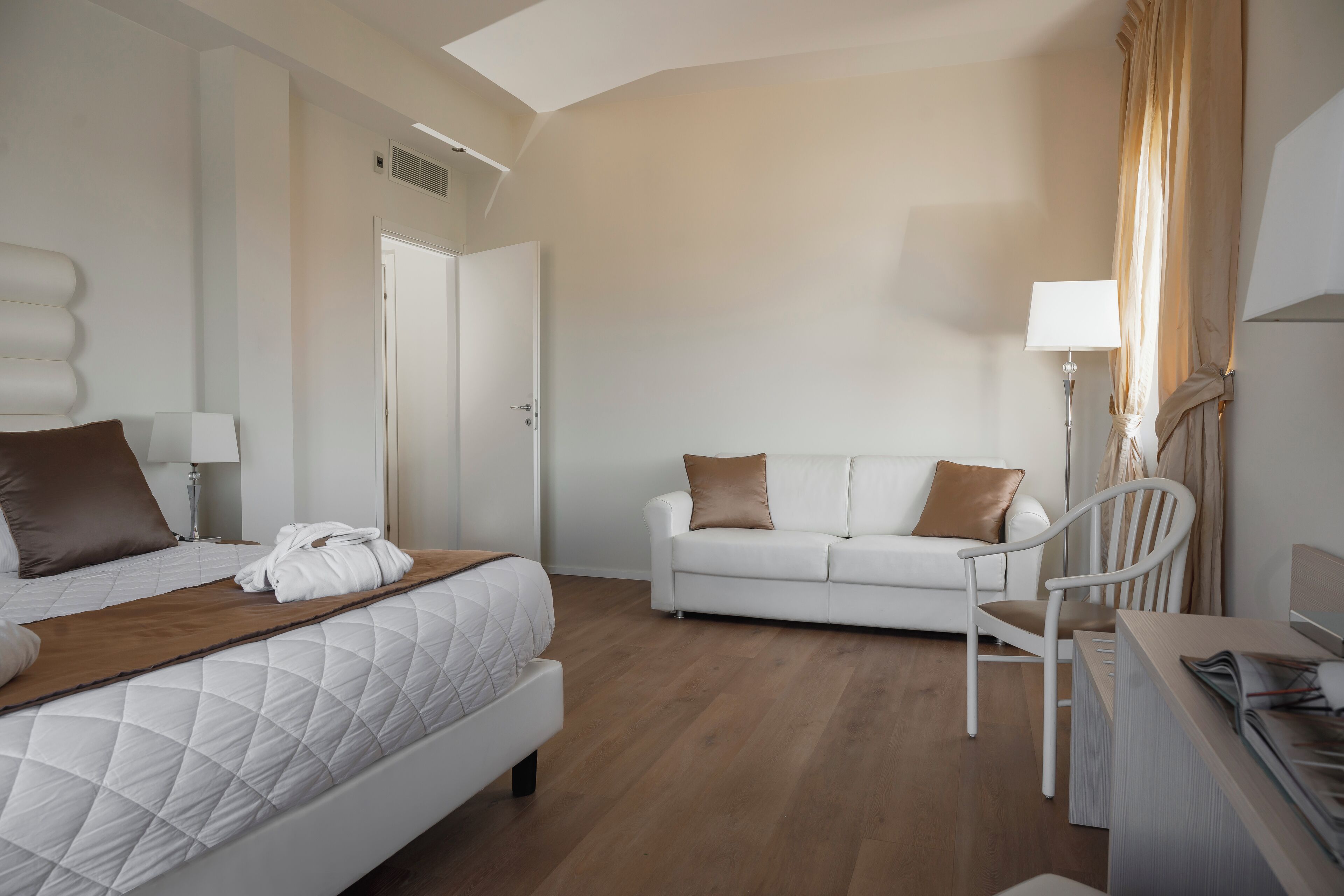 Una camera d'albergo con un letto, un divano bianco, una scrivania e una sedia.