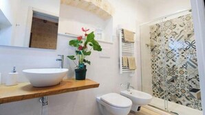 Een badkamer met een groot wit wastafelmeubel, een toilet en een bidet. Er is een douche met betegelde wanden en een handdoekhouder.