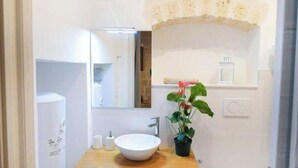 Een badkamer met een houten wastafelmeubel, een witte wasbak, een spiegel en een potplant.
