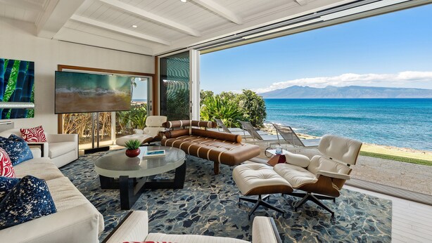A modern living room with a large window overlooking a beach and ocean. - SUMMER SALE! Discover paradise in a 3-bedroom oceanfront getaway - Alaeloa 28 (Lahaina)