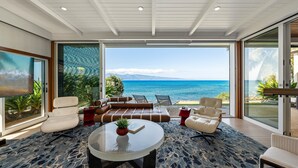 A modern living room with a large glass door leading to a balcony overlooking the ocean. - SUMMER SALE! Discover paradise in a 3-bedroom oceanfront getaway - Alaeloa 28 (Lahaina)