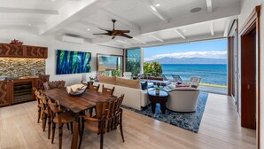 A spacious living area with a large wooden dining table, comfortable seating, and a view of the ocean. - SUMMER SALE! Discover paradise in a 3-bedroom oceanfront getaway - Alaeloa 28 (Lahaina)
