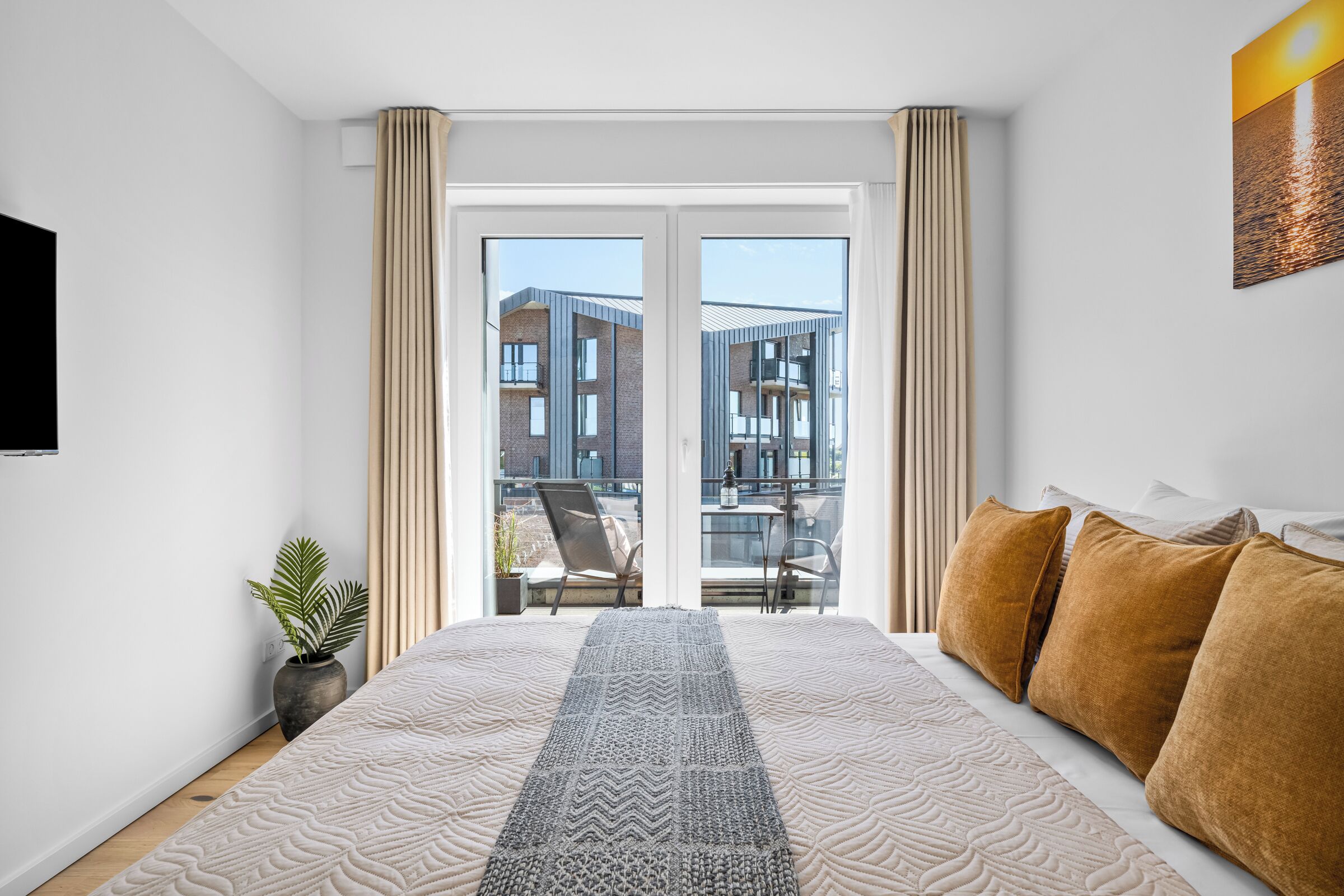 A modern bedroom with a large bed, a view of a building through the window, and a potted plant.
