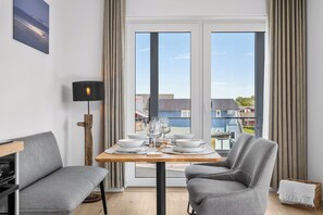 Un coin repas avec une table dressée pour deux personnes, un canapé, une lampe et une vue sur l’extérieur.
